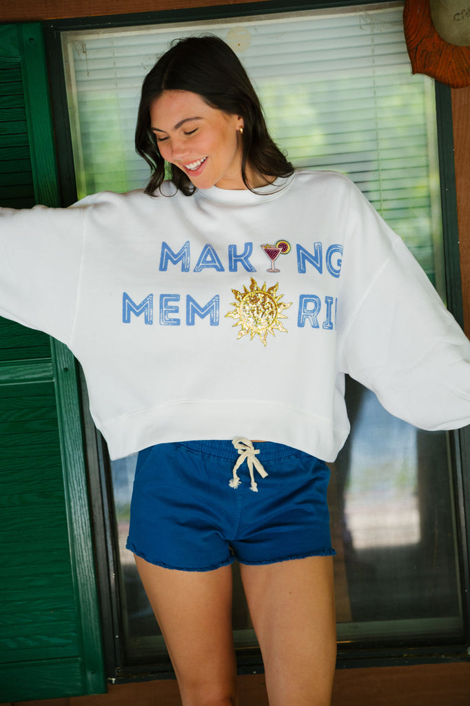 White cropped pullover with "making memories" in blue printed lettering, sequin sun patch, and sequin martini patch. 