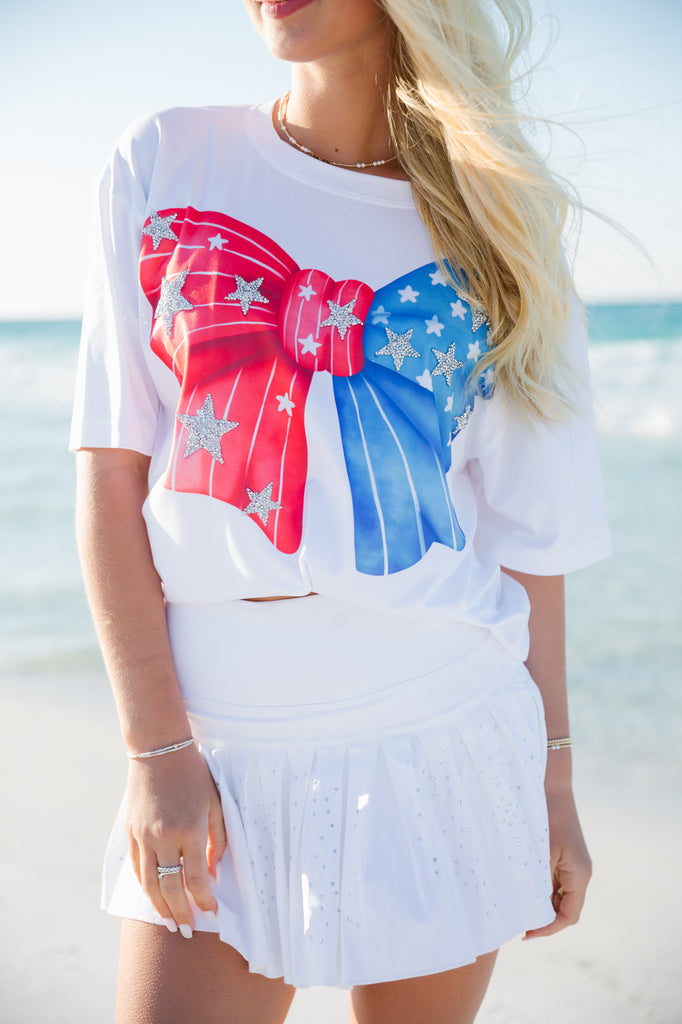 White t-shirt with a red and blue bow print and silver stars