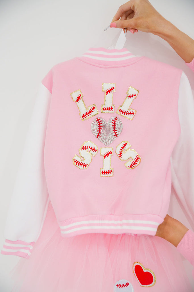 Kids pink and white varsity jacket with "lil sis" in baseball terry letters and a rhinestone baseball heart. 