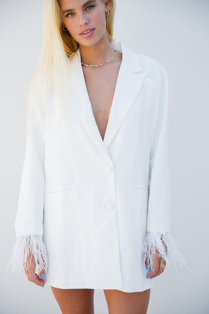 White blazer with feather sleeve cuffs and "Bride" across the back. 