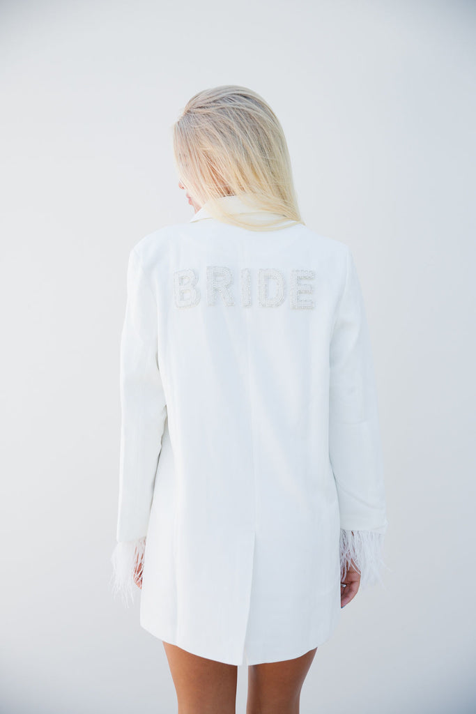 White blazer with feather sleeve cuffs and "Bride" across the back. 