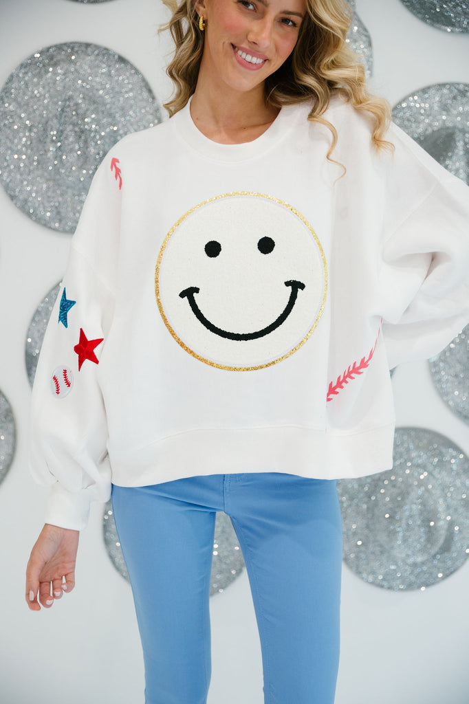 White cropped pullover with a smiley face patch and baseball patterns