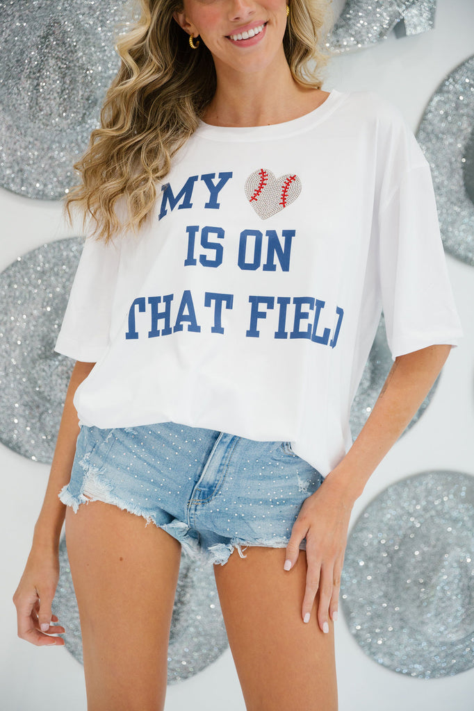 White t-shirt with "My Heart Is On That Field" in a blue print with a baseball heart patch