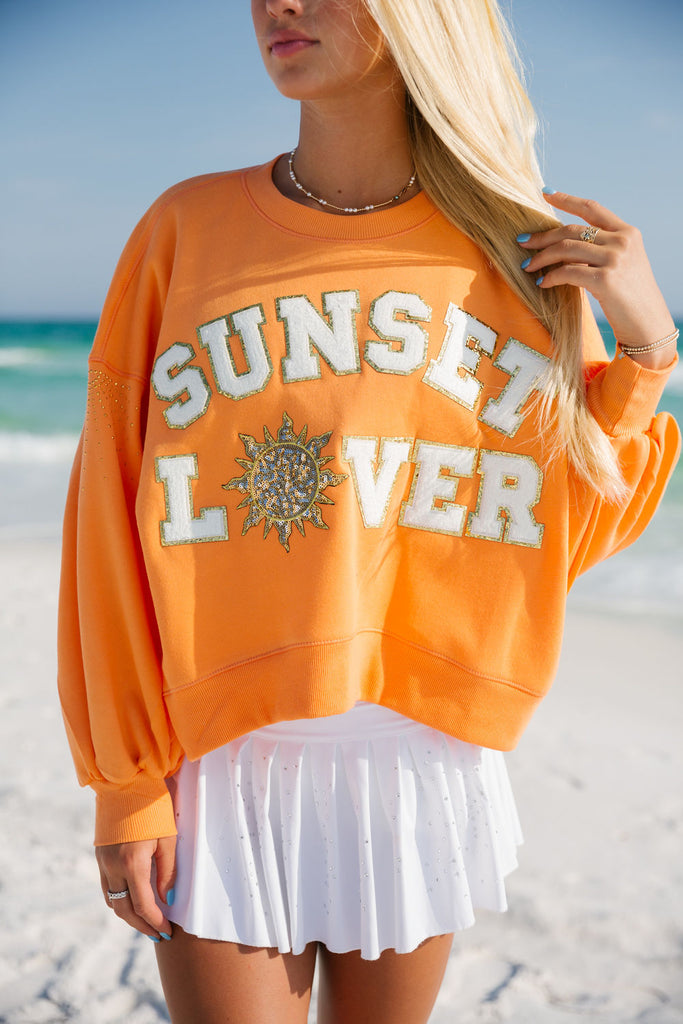 Orange pullover with "Sunset Lover" across the front with a sequin sun patch. 