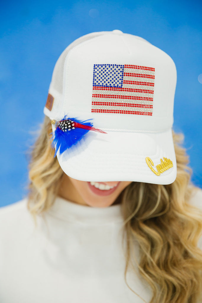 White trucker hat with American flag patch, gold Caddie patch, and feathers