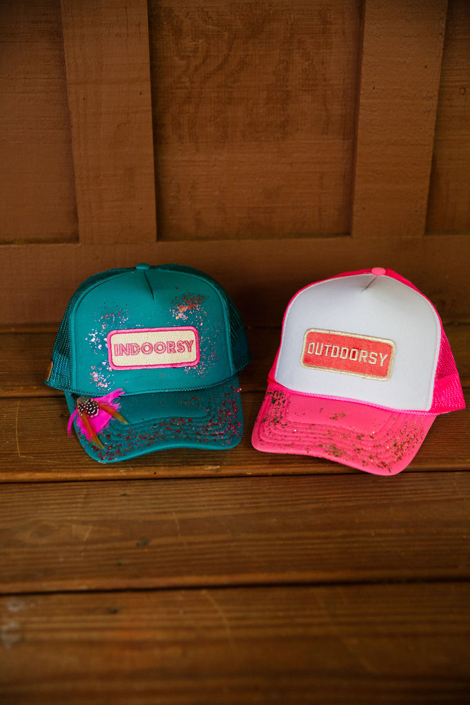 Turquoise trucker hat with indoorsy patch, pink feathers, and pink glitter spray. 