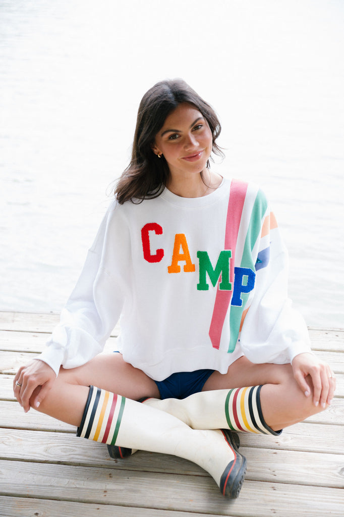 White cropped pullover with "camp" in colorful varsity lettering and a colorful print design. 