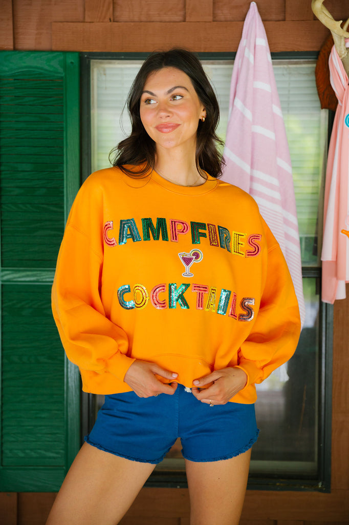 Orange cropped pullover with Campfires and Cocktails in sequin lettering with a cocktail patch
