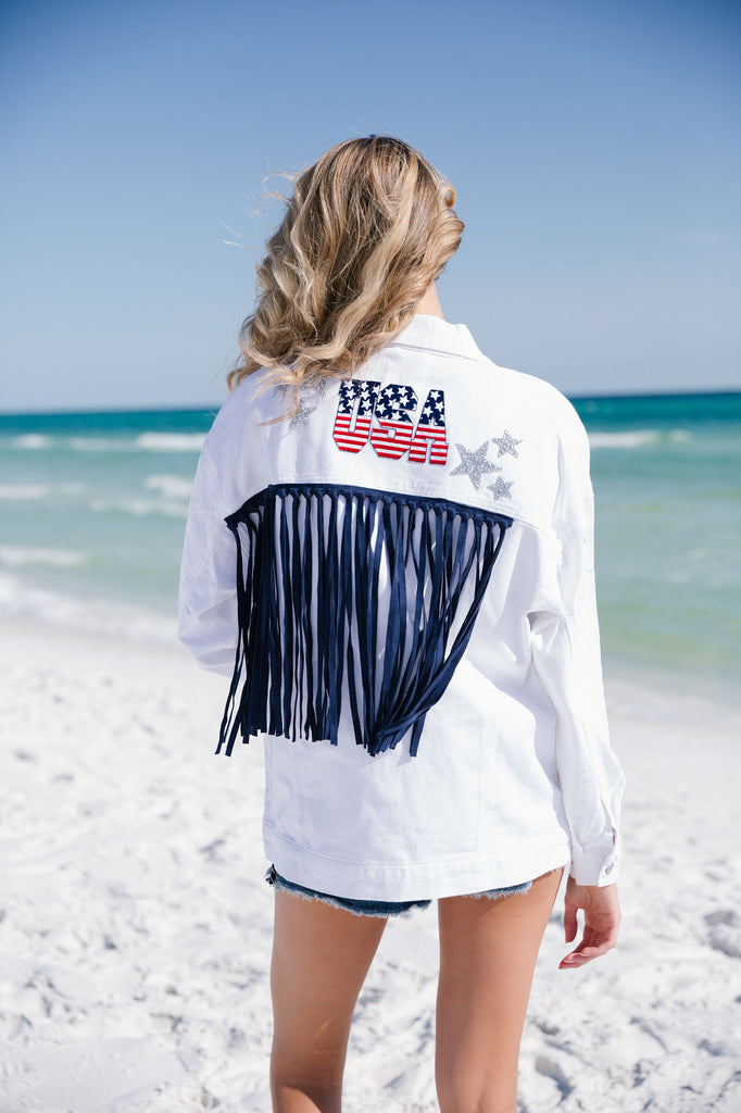 White denim jacket with American flag "USA" letters, silver stars, and navy fringe on the back