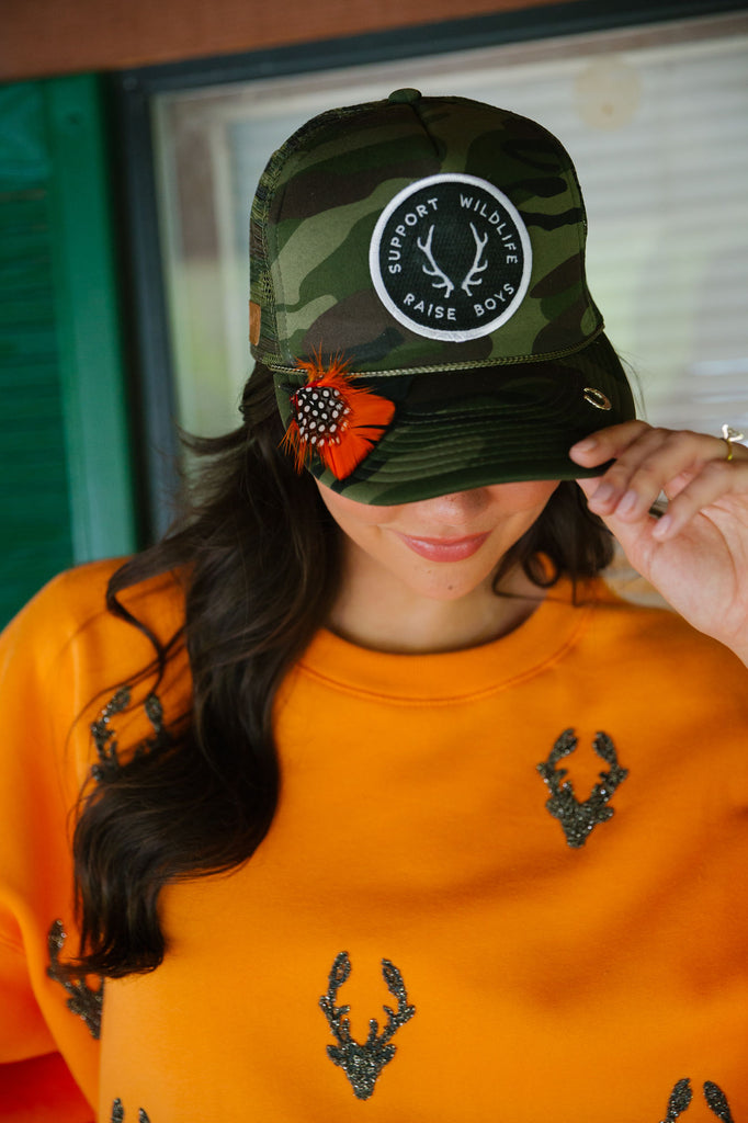 Camo trucker with feathers, pins, and Support Wildlife Raise Boys patch