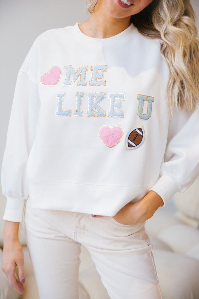 White pullover "love me like you love football" in mini light blue terry lettering with terry hearts and a football patch. 