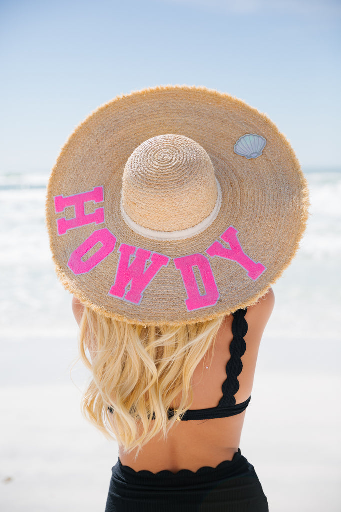 Straw sun hat with Howdy in pink varsity letters and a seashell patch
