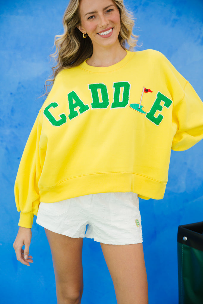 Yellow pullover with "caddie" in green varsity lettering and 18th hole patch. 