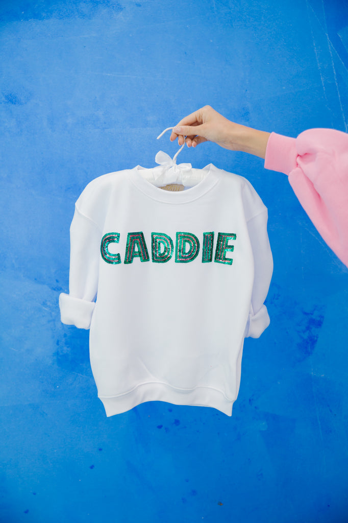 Kids white pullover with "caddie" in green sequin lettering. 