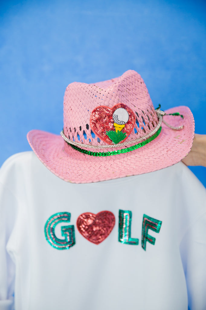 Pink cowgirl hat with a red sequin heart patch, golf tee patch, green sequin band, and a white diamond band. 