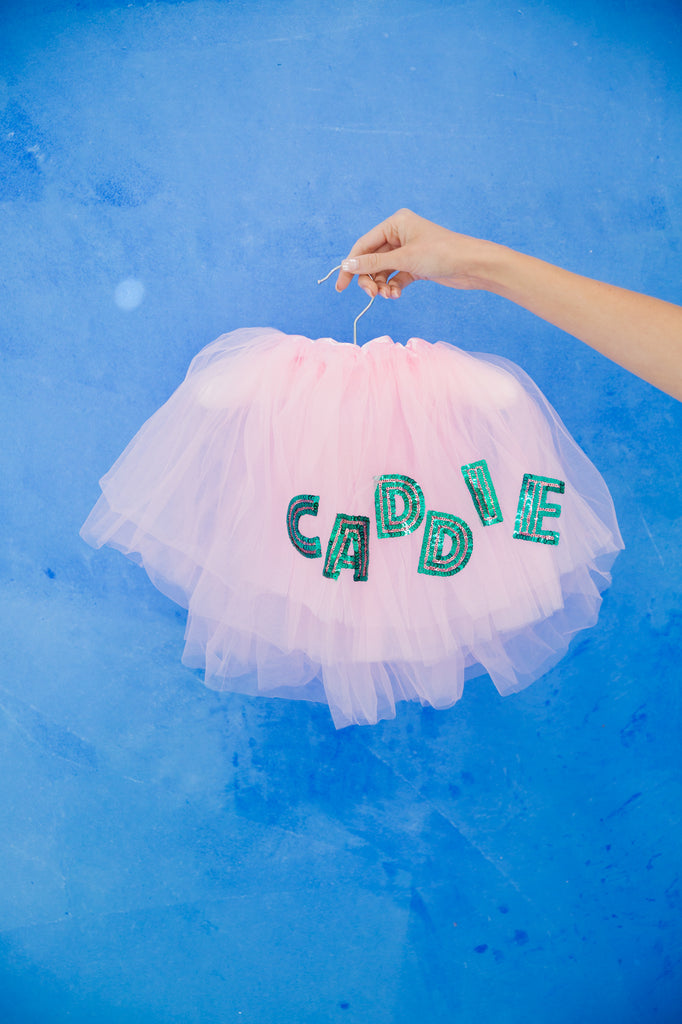 Pink tutu with "caddie" in green sequin lettering. 