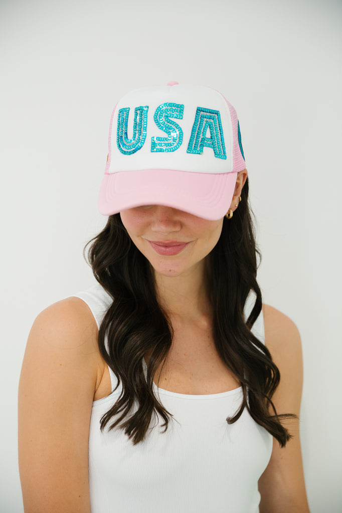 Pink and white trucker hat with blue sequin "USA" letters and blue smiley face on the side