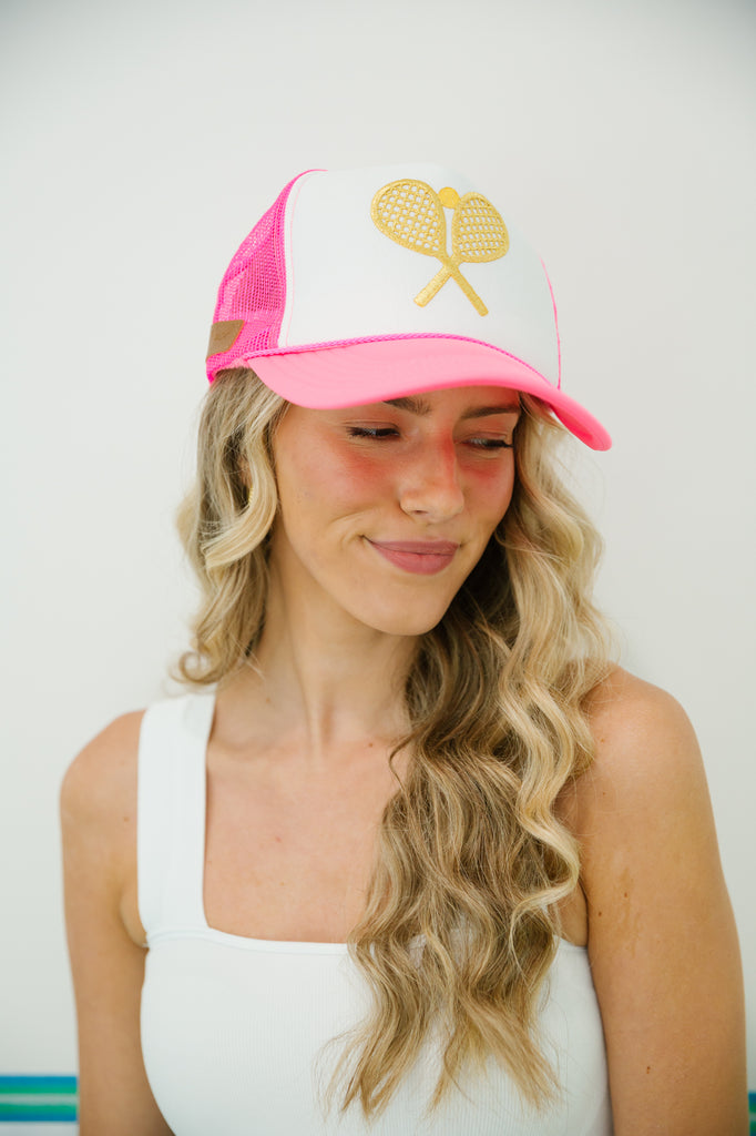 Hot pink and white trucker hat with gold tennis racket patch.  