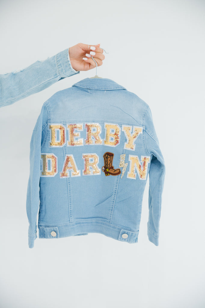 Kids denim jacket with "derby darlin" in gold sequin lettering, rhinestone lightening bolt patch, and a cowboy boot patch. 