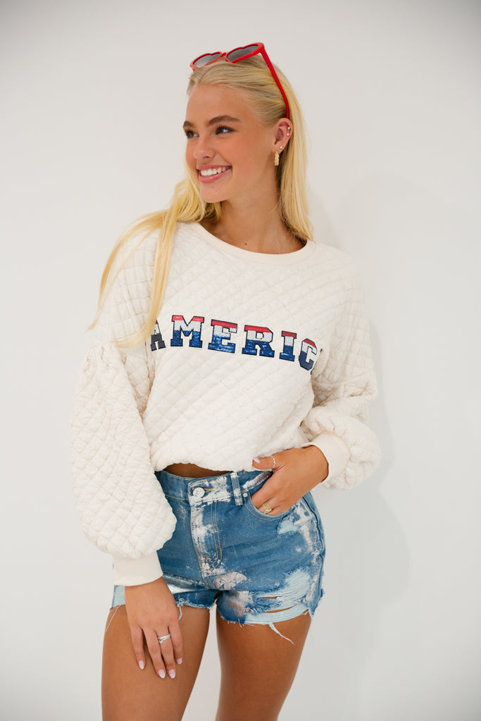 Cream quilted pullover with red, white, and blue "America" letters