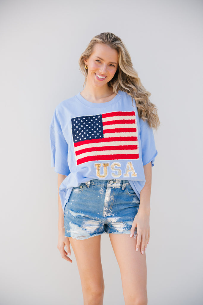 Light blue t-shirt with an American flag on the front with gold sequin "USA" letters
