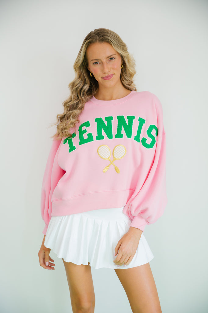 Pink cropped pullover with Tennis in green varsity letters and a gold tennis racket patch