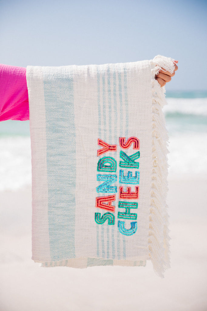 Beige and blue beach towel with Sandy Cheeks in colored sequin letters